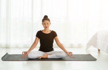 Middle aged women practicing yoga in Easy seat pose or Sukhasana with with mudra. Meditation with yoga in white bedroom after wake up in the morning. Concept of exercise, relaxation and healthcare. clipart