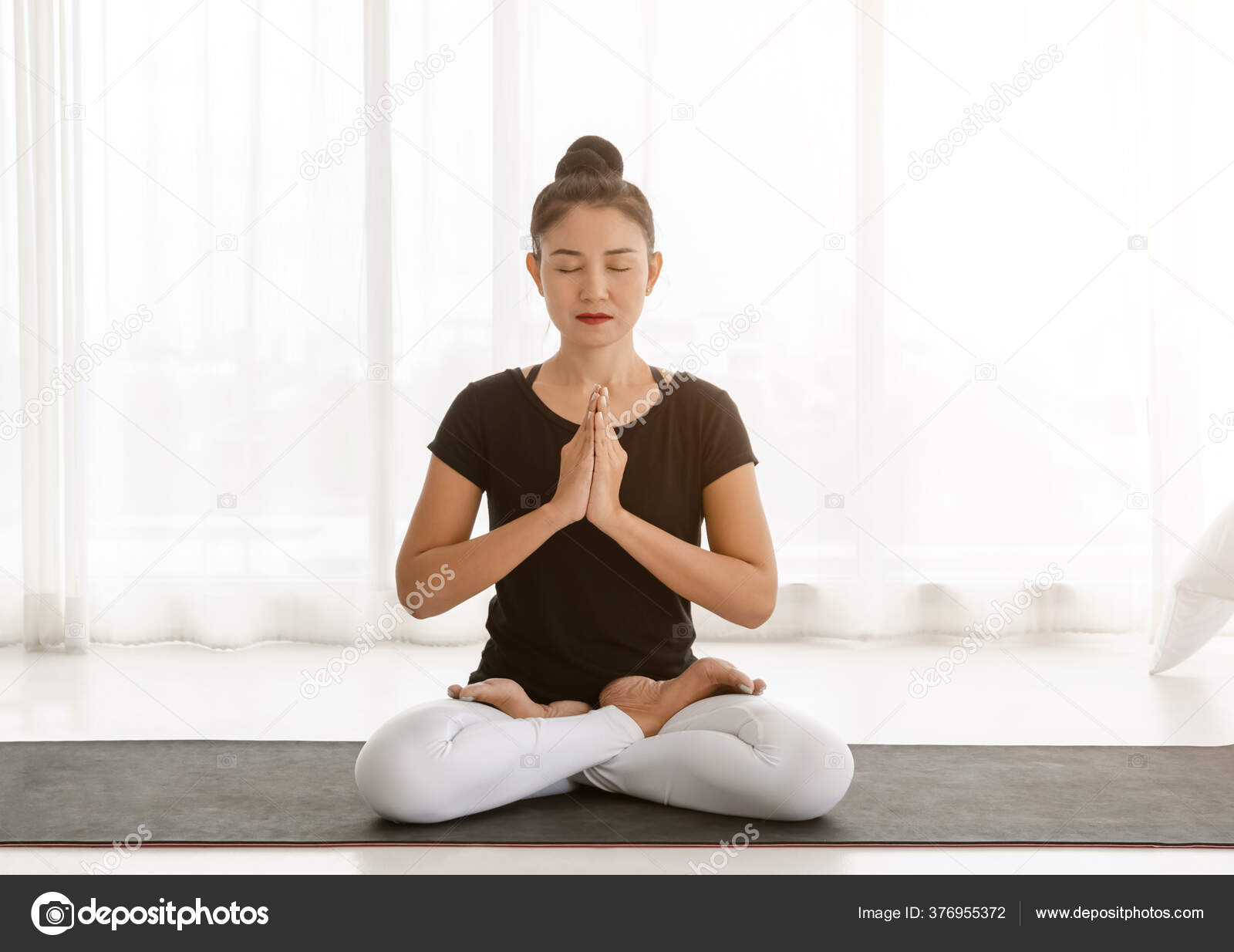 Attractive young woman exercising and sitting in yoga lotus position while  resting at home | Elle Well Studio + Wellness