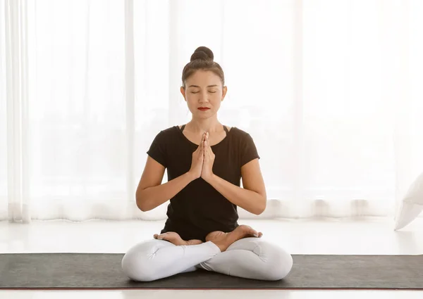 Middle aged women practicing yoga in Lotus pose or Padmasana with raised hands namaste. Meditation with yoga in white bedroom after wake up in the morning. Concept of exercise, relaxation and healthcare.
