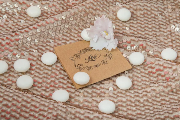 the inscription love with a white violet, white round sweets on a shiny gold fabric