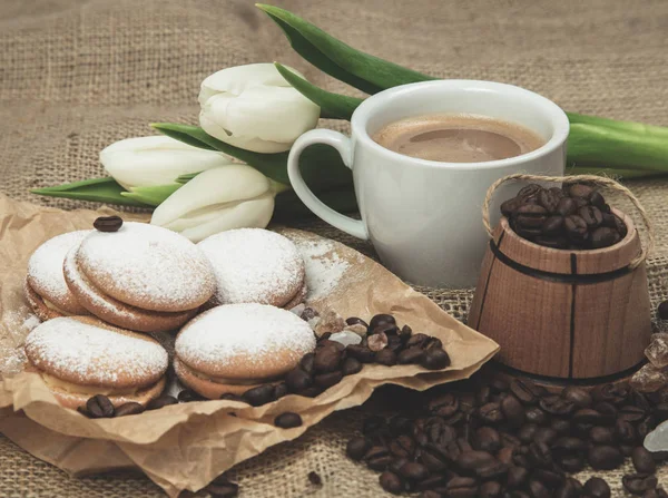 spring still-life from a cup of coffee with milk, biscuits, a bouquet of white tulips on a rough background