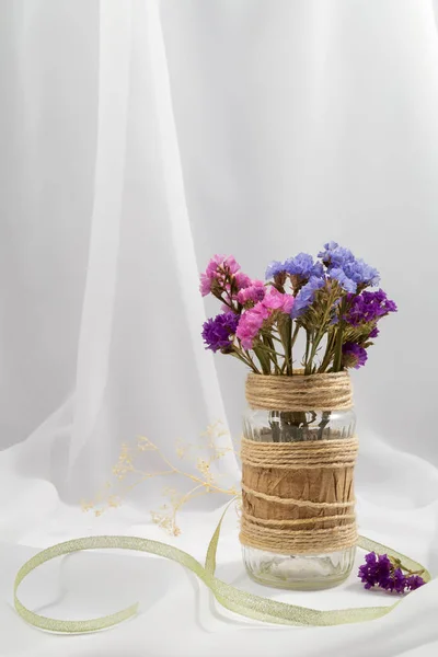 el ile bir cam kavanoza kuru pembe, mavi ve mor çiçekler buket dekore edilmiş