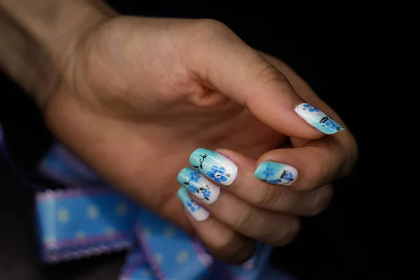 Niebieski manicure z kwiatowym wzorem i kokardą w dłoni — Zdjęcie stockowe
