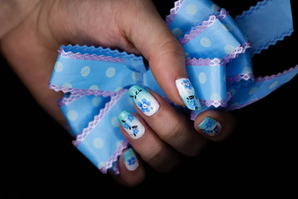 Niebieski manicure z kwiatowym wzorem i kokardą w dłoni — Zdjęcie stockowe