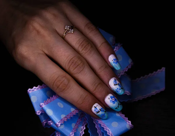 Blue manicure with a flower pattern, and a bow in hand, with a g — Stock Photo, Image