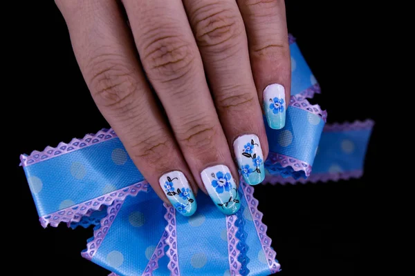 Manucure bleue avec un motif de fleurs, et un arc à la main — Photo