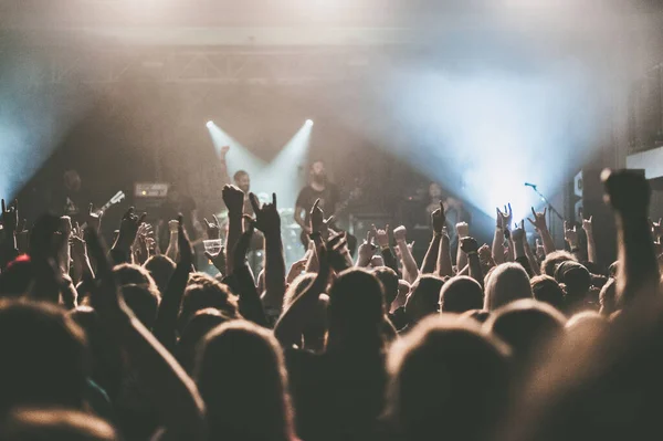 Crowd at a concert raising their hands up with the band blurred in the background toned