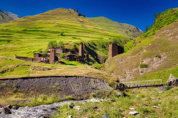 Gürcistan 'ın Tusheti bölgesindeki Omalo antik dağlık köyü. Parlak mavi gökyüzü, taş evler ve kuleler, yeşil yemyeşil çimenler ve hızlı bir nehir..