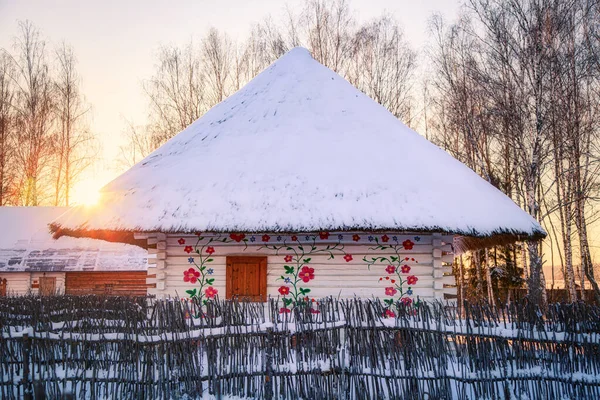 Traditionelle alte russische Hütte mit Strohdach, das mit Schnee bedeckt ist. kaltes Winterwetter und Sonnenuntergang. — Stockfoto