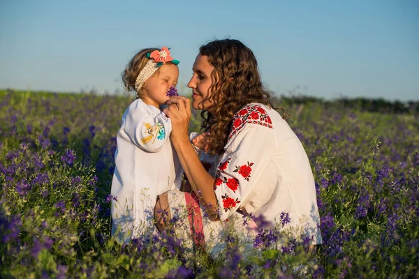 Smiling mother and little daughter on nature in a field of poppies, girl is holding flowers. Happy people outdoors — Stock Photo, Image