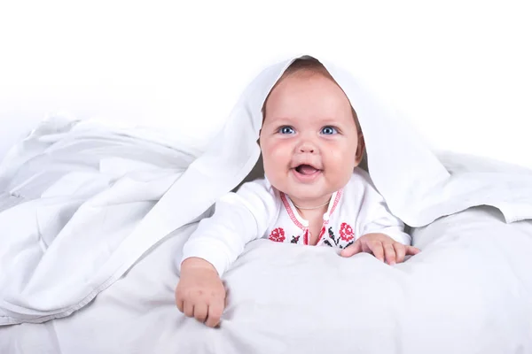 Chica feliz escondida en la cama bajo una manta blanca o cobertor. Chica en la cama. Niño en la cama. aislado sobre fondo blanco — Foto de Stock