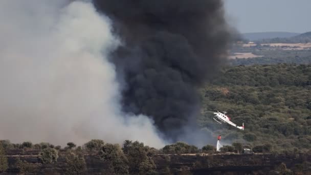 Вертолет на горизонте бросает воду в огонь с огромным дымом — стоковое видео