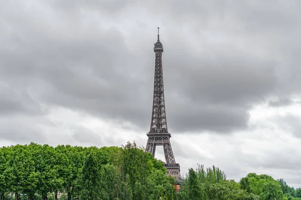 A Torre Eiffel emergindo sobre árvores com nuvens tempestuosas — Fotografia de Stock
