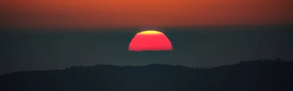 Pôr do sol com céu laranja e sol atrás da névoa sobre a cordilheira — Fotografia de Stock