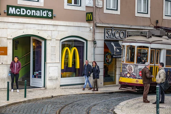 Lisabon - 9. dubna: Neznámí lidé pěšky, talk a čekání, zatímco slavná 28 linka tramvaje se objeví v obraze na 9 dubna 2018 v Lisabonu, Portugalsko — Stock fotografie