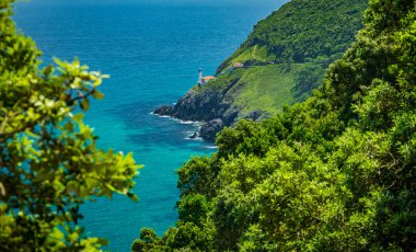 Yamaçtaki parlak okyanuslu deniz fenerinin uzak bir görüntüsü.