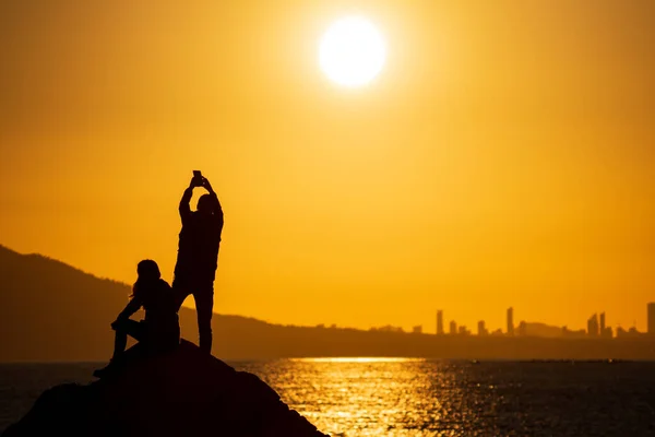 Couple taking photos at sunset over city skyline — Stock Photo, Image