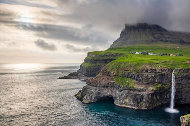 Gasadalur şelalesinin geniş açısı alacakaranlıkta bulutlarla birlikte.
