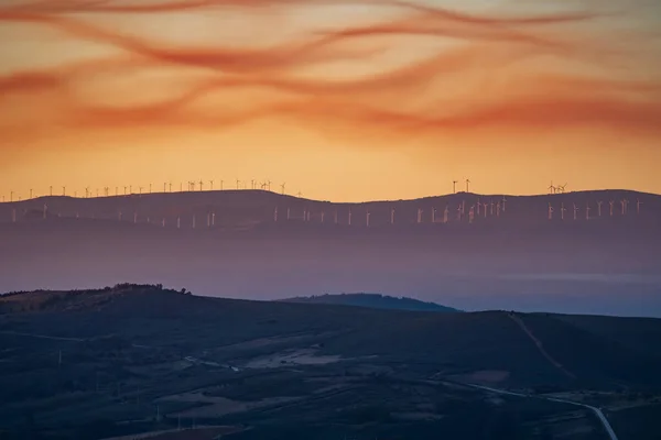 Campo com moinhos de vento no fundo e céu nublado ao pôr do sol — Fotografia de Stock