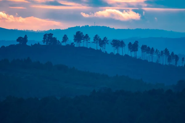 オレンジの空と層に多くの青い丘の夕日 — ストック写真