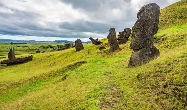 Bulutlu gökyüzünün altındaki yamaçta bükülmüş moais 'ler