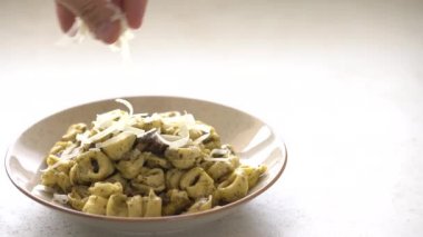 Noktalı tabakta tortellini al pesto üzerine peynir dilimleri.