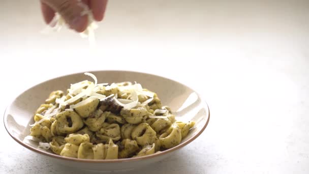 Насыпать кусочки сыра на тортеллини и песто на тарелку — стоковое видео