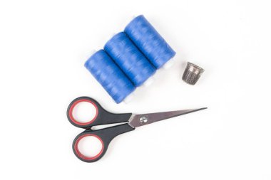 Mavi dikiş ipliği küçük siyah makas ve beyaz zemin üzerine metal yüksük