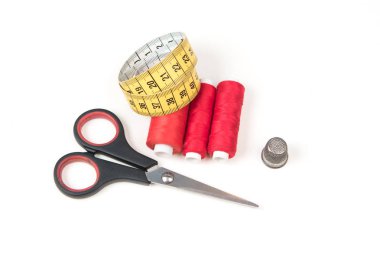 Dikiş aksesuarları ve araçlar. Kırmızı dikiş ipliği, siyah makas, ölçüm bandı ve yüksük beyaz zemin üzerine sarı. Tekstil arka plan