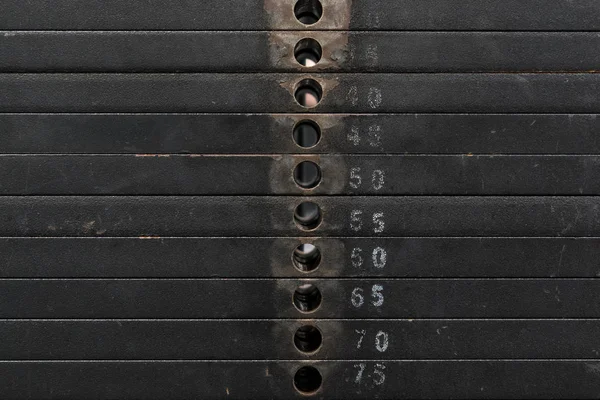 Old and used black weight stack with white numbers in a gym. Rusty flat metal weights. Metal weights as background or wallpaper