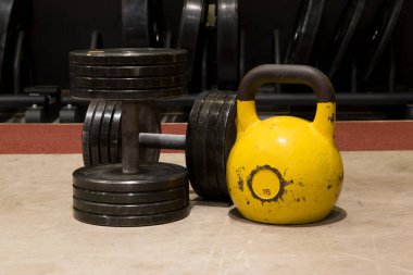 İki eski ve kullanılan spor salonu siyah metal dumbbells ile ahşap bir zemin üzerinde büyük sarı kettlebell