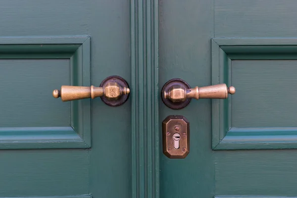 Golden door handles on green wooden doors. Old door handle
