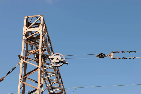 Train or railway power line support. Railway power lines with high voltage electricity on metal poles against blue sky.