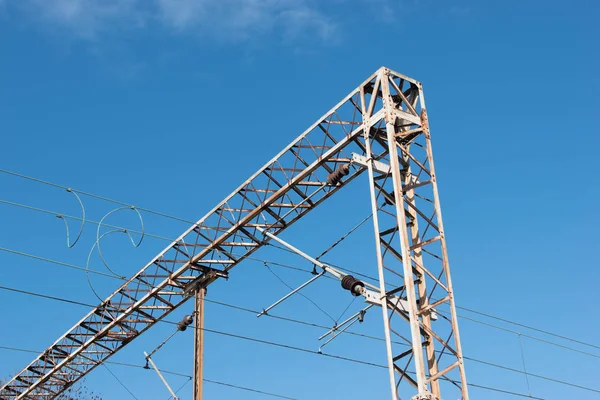 Train or railway power line support. Railway power lines with high voltage electricity on metal poles against blue sky.