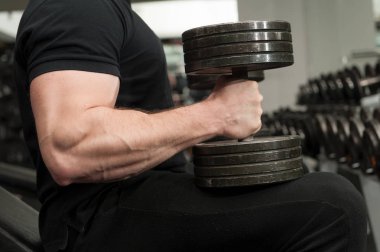 Kaslı vücut geliştirmeci adam büyük siyah demir dumbbells bir spor salonunda. Bir spor salonunda egzersiz büyük el kasları olan adam. Spor salonu ve fitness ayrıntıları