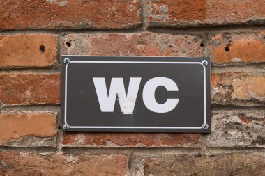 Tuvalet Wc eski kırmızı tuğla duvara imzala. Siyah metal plaka beyaz Wc işareti. Açık oturum.