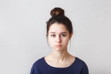 portrait of a pimply teenage girl in a blue T-shirt on a gray background, sad face clipart