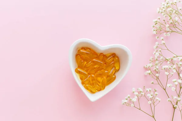 Health prevention concept, heart-Cup with a bunch of different pills and vitamins and omega, on pink background, top view with gypsophila