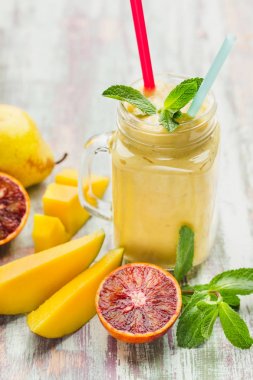 Bir bardak meyve yüzlü ahşap bir masa üzerinde dilim mango kırmızı portakal, armut, nane fışkın. Sağlıklı beslenme kavramı.