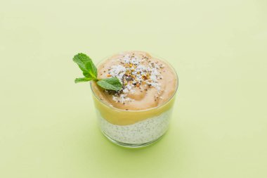 Bir bardak meyve yüzlü hindistancevizi talaşı ve chia tohum ve yeşil zemin üzerine nane fışkın