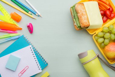 Ahşap bir mavi masa, bir not defteri, renkli kalem, cetvel, marker, planya, metin için yer üzerinde çeşitli ileti örneği yığını. Lezzetli okul beslenme çantası, sandviç ve meyve. Çocuklar okul için hazırlık kavramı.