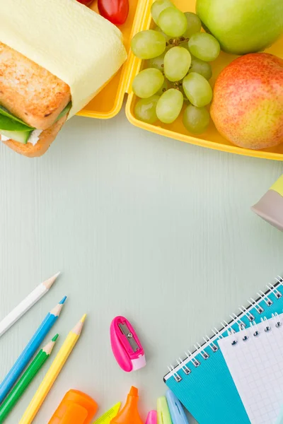 Ένα σωρό από διάφορες επιστολόχαρτο σε ένα ξύλινο τραπέζι μπλε, ένα σημειωματάριο, χρωματιστά μολύβια, χάρακα, δείκτη, μηχανή πλανίσματος, χώρο για το κείμενο. Νόστιμο σχολικό κολατσιό, σάντουιτς και φρούτα. Η έννοια της προετοιμασίας των παιδιών για το σχολείο. — Φωτογραφία Αρχείου