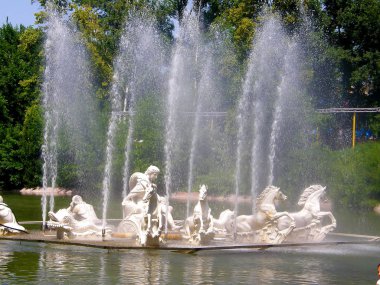 Parktaki su yüzeyindeki fıskiyeler, ağaçların arka planında çalışan bir çeşme.