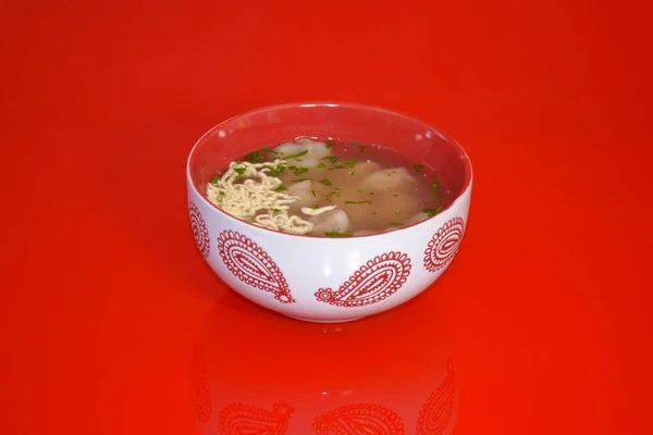 Kafeterya için çekilen fotoğrafta yemek, kırmızı arka planda ulusal bir deseni olan çorbalı börekler var.