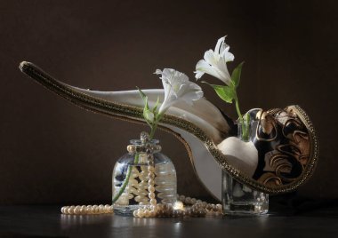 Gagalı Venedik Karnavalı Veba Doktoru maskesi, küçük şişelerde iki Alstroemeria çiçeği ve arka planda bir dizi inciyle Retro tarzı sakin bir hayat. Seçici ve yumuşak odak. 