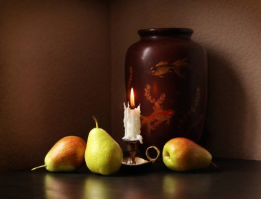 Üç tatlı olgun armut, yanan mumlu şamdan ve sade arka planda duran güzel bir vazo ile sakin bir hayat. Metnin için seçici yumuşak odak ve boşluk.