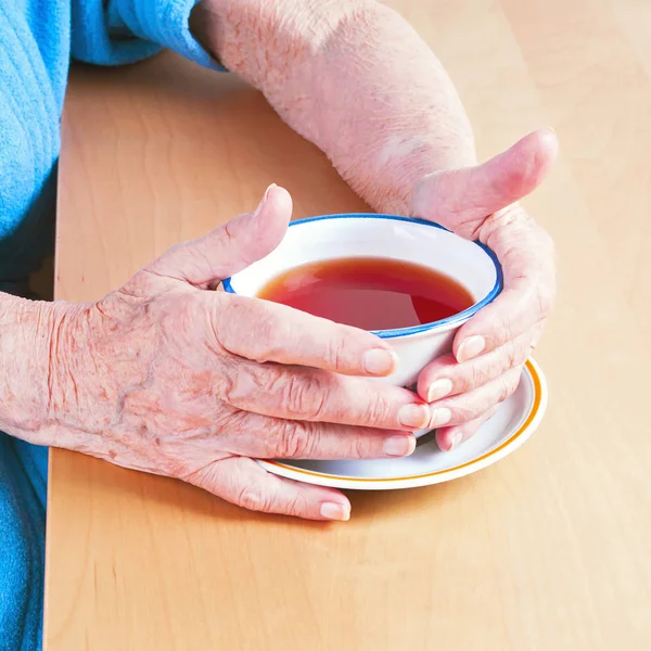 Oude handen met een kopje thee — Stockfoto