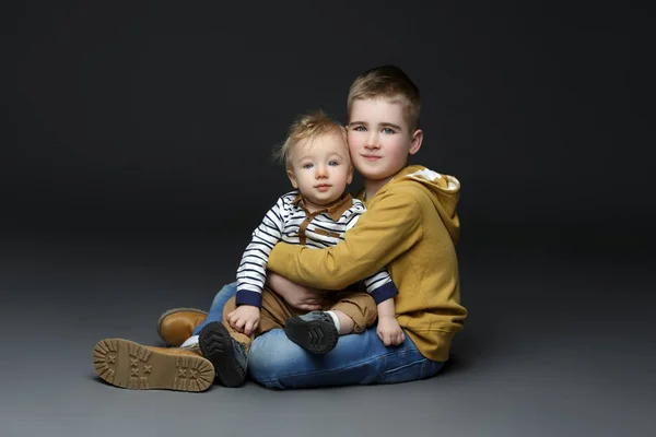 Dois irmãos de jeans sentados no chão — Fotografia de Stock