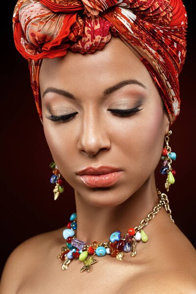 Beautiful mulatto young woman with orange turban on head. beauty shot on dark background. copy space.