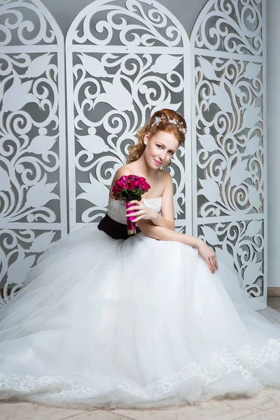 beautiful red hair young woman in white wedding gown with wide dark purple belt. bride with fashion hairstyle. studio shot.